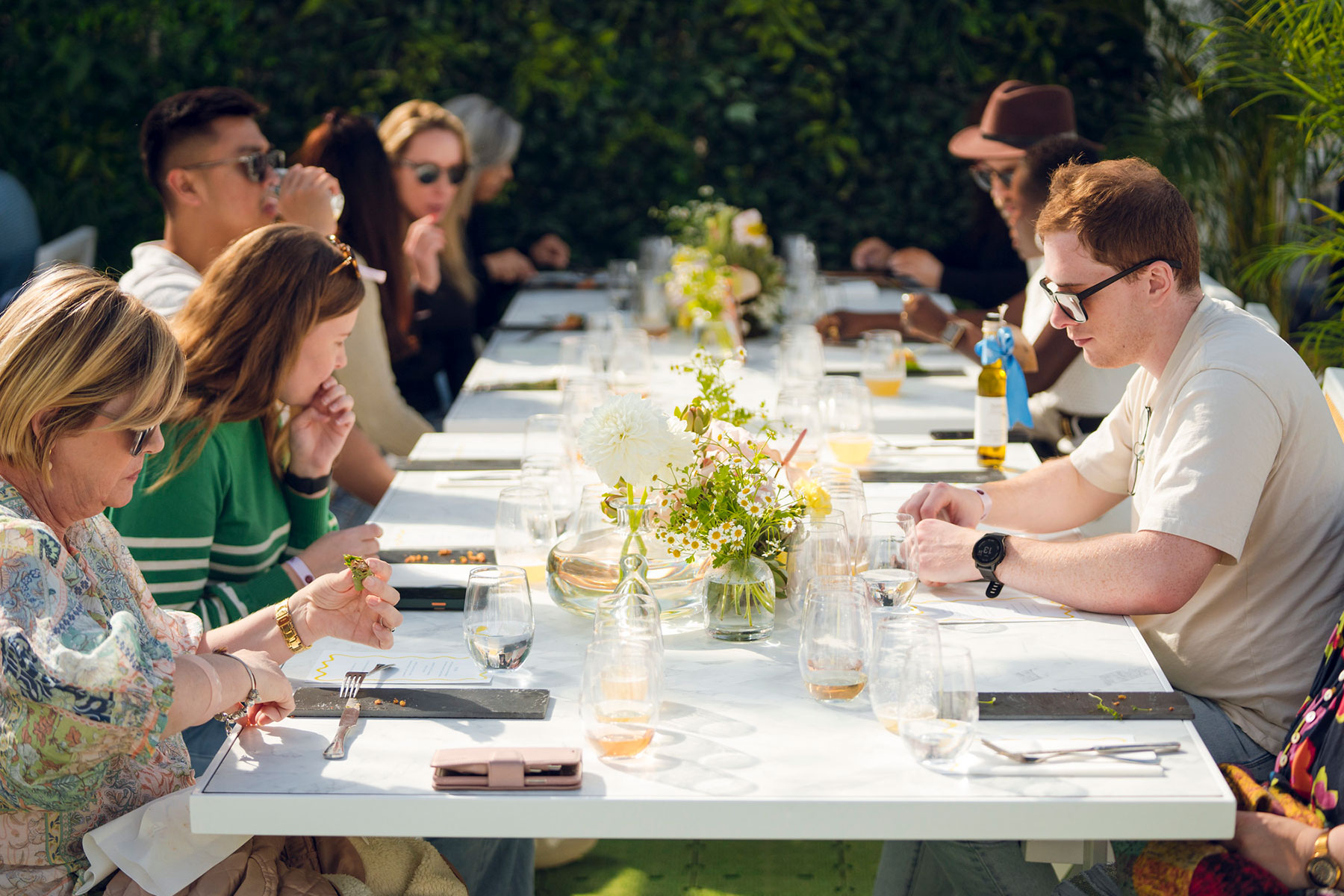Several people sat at a long table set with flowers and glasses of beverages