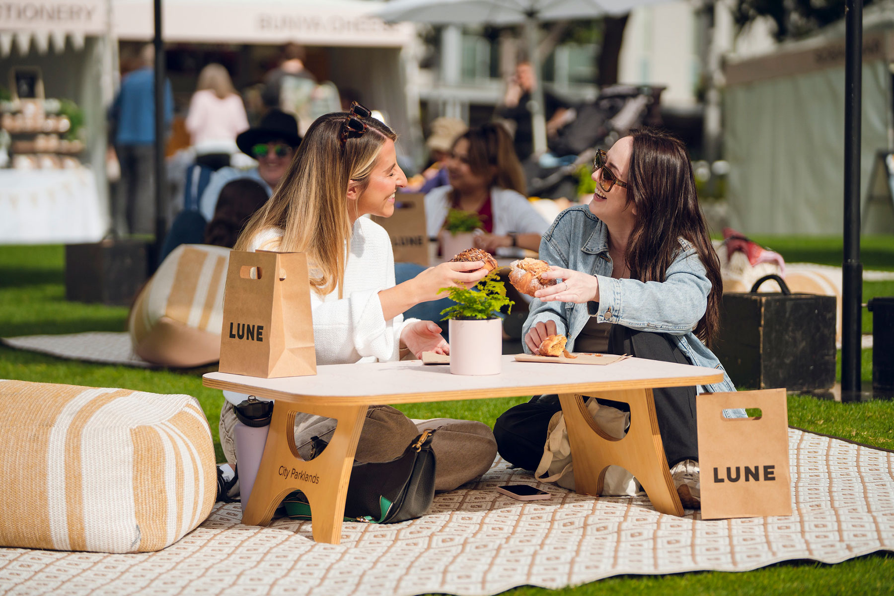 Two people sat on a picnic rug at a low picnic table enjoying LUNE croissants