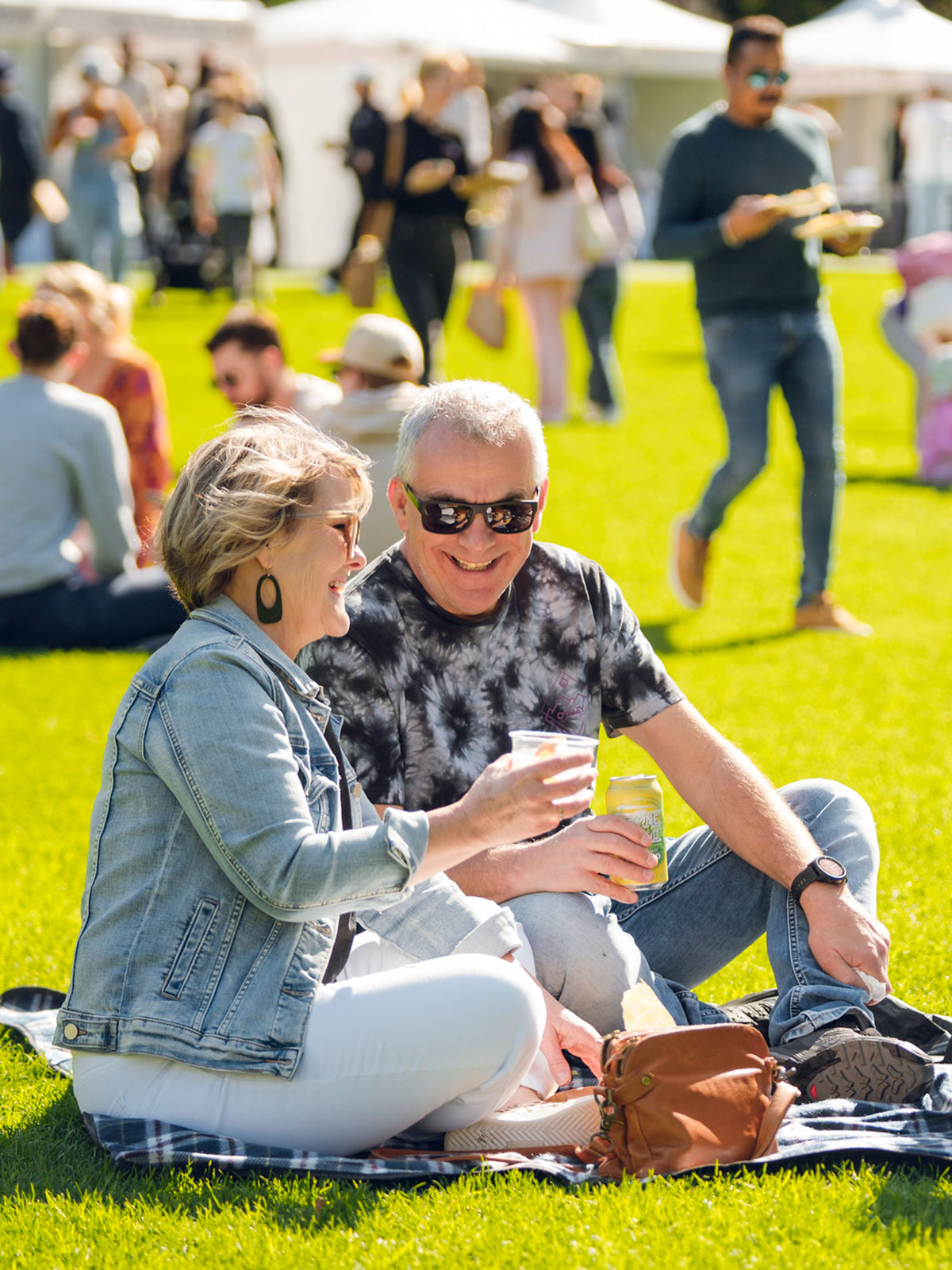 Couple sat on a picnic rug on the grass on a sunny day enjoying a beverage