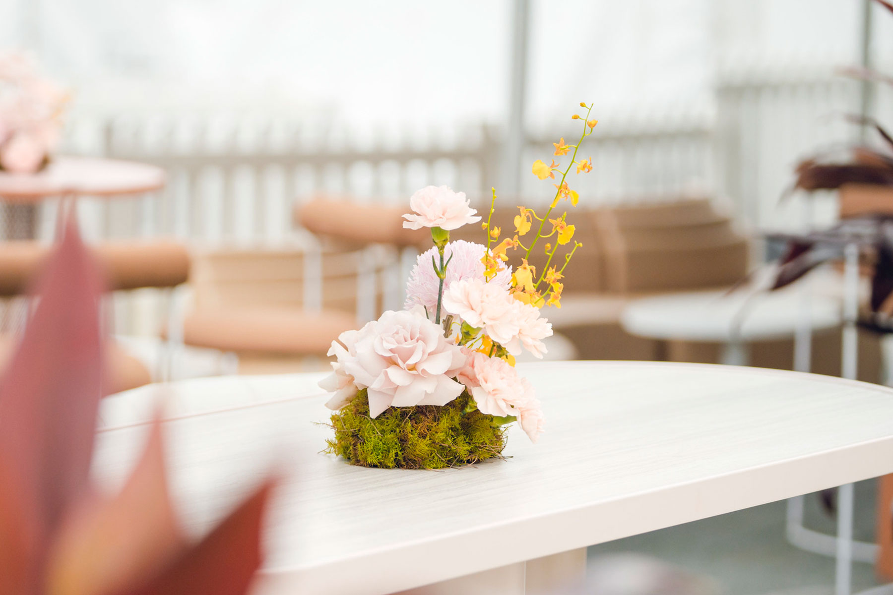 Floral table arrangement with pale pink rose pale pink carnation and small mild yellow orchids