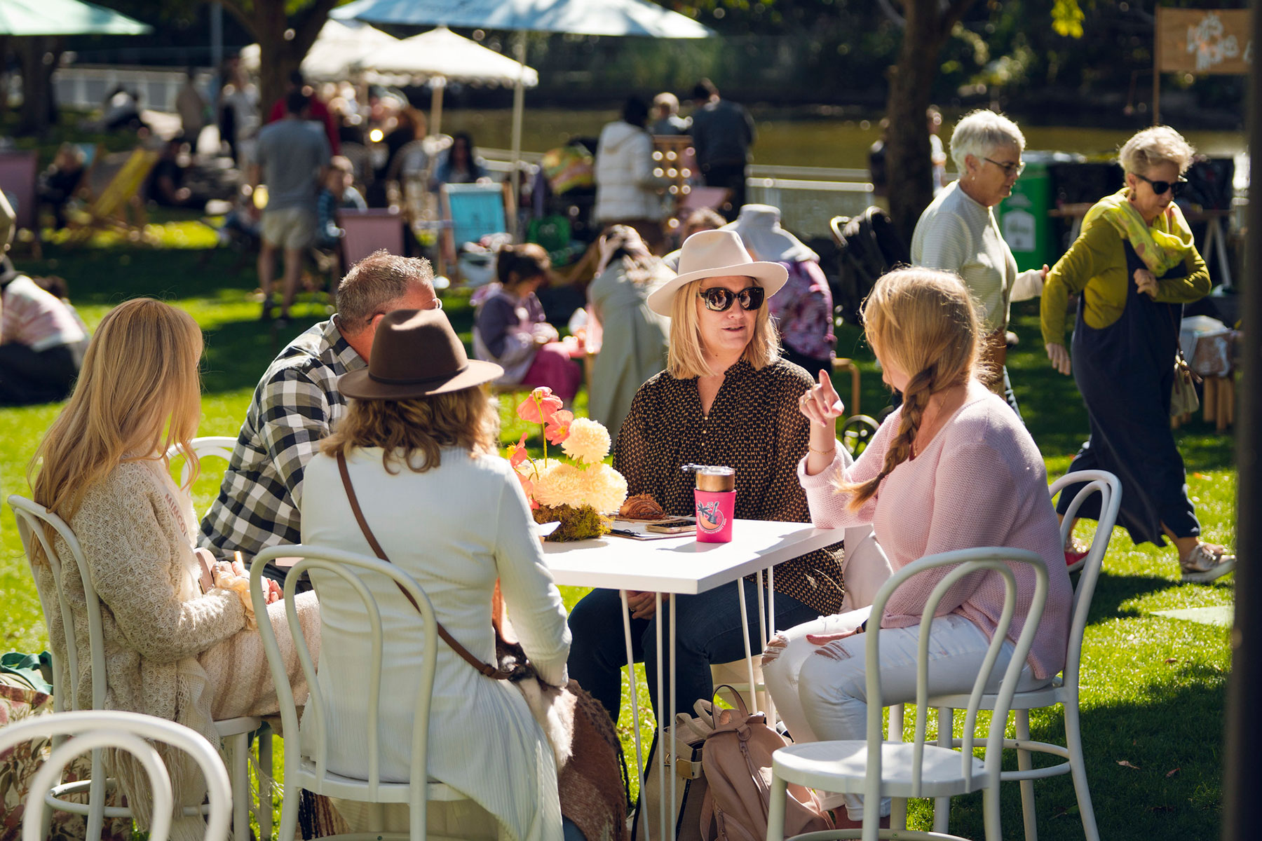 Friends seated around a white table on the grass on a sunny day enjoying a conversation