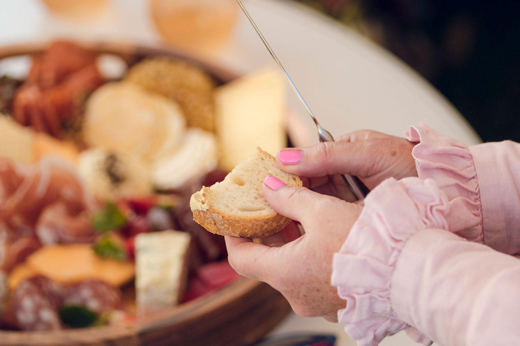 Hands breaking bread with cheese platter in the background
