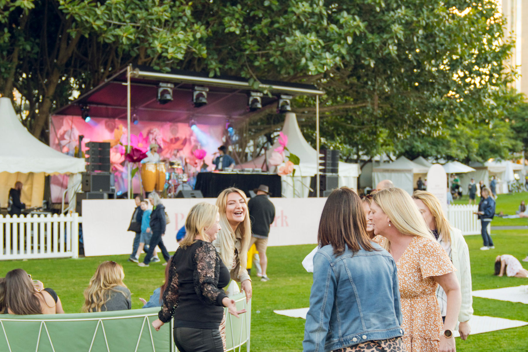 People standing and dancing in front of a stage outdoors in a park