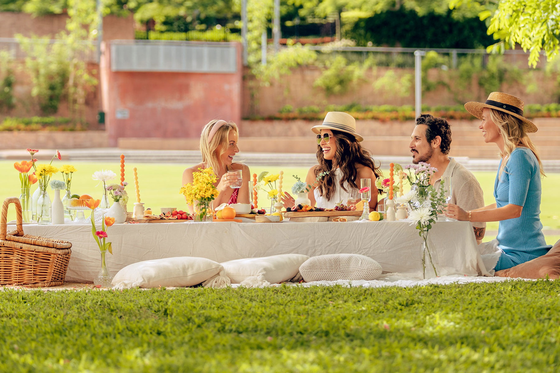 Four people sat at an elegatnly styled picnic table enjoying a pcinic with food drinks and floral arrangement